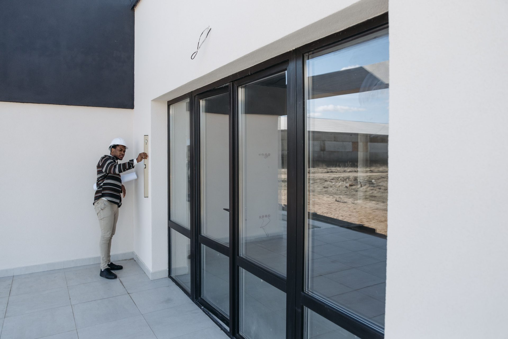 Architekt mit Schutzhelm inspiziert Glastür im Neubau eines modernen Hauses.