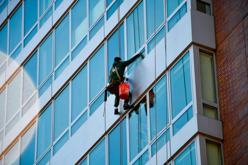 Ein Fensterputzer reinigt die Außenfassade eines hohen Gebäudes.